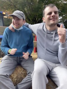 Two people sitting together, both smiling. One of them is giving a thumbs up. 
